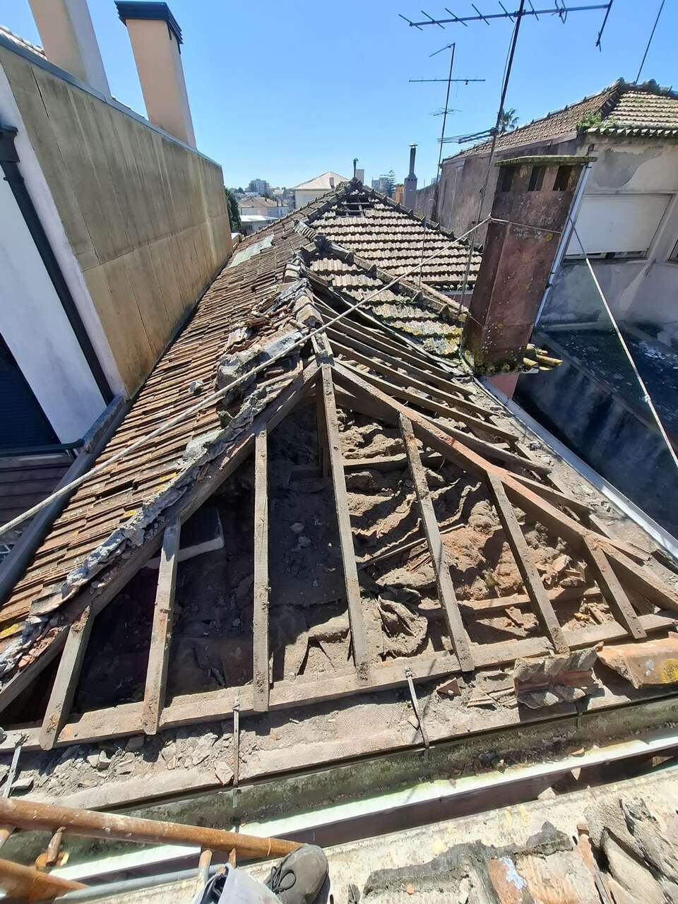 Estrutura antiga do telhado exposta, com telhas por remover, vista da cidade