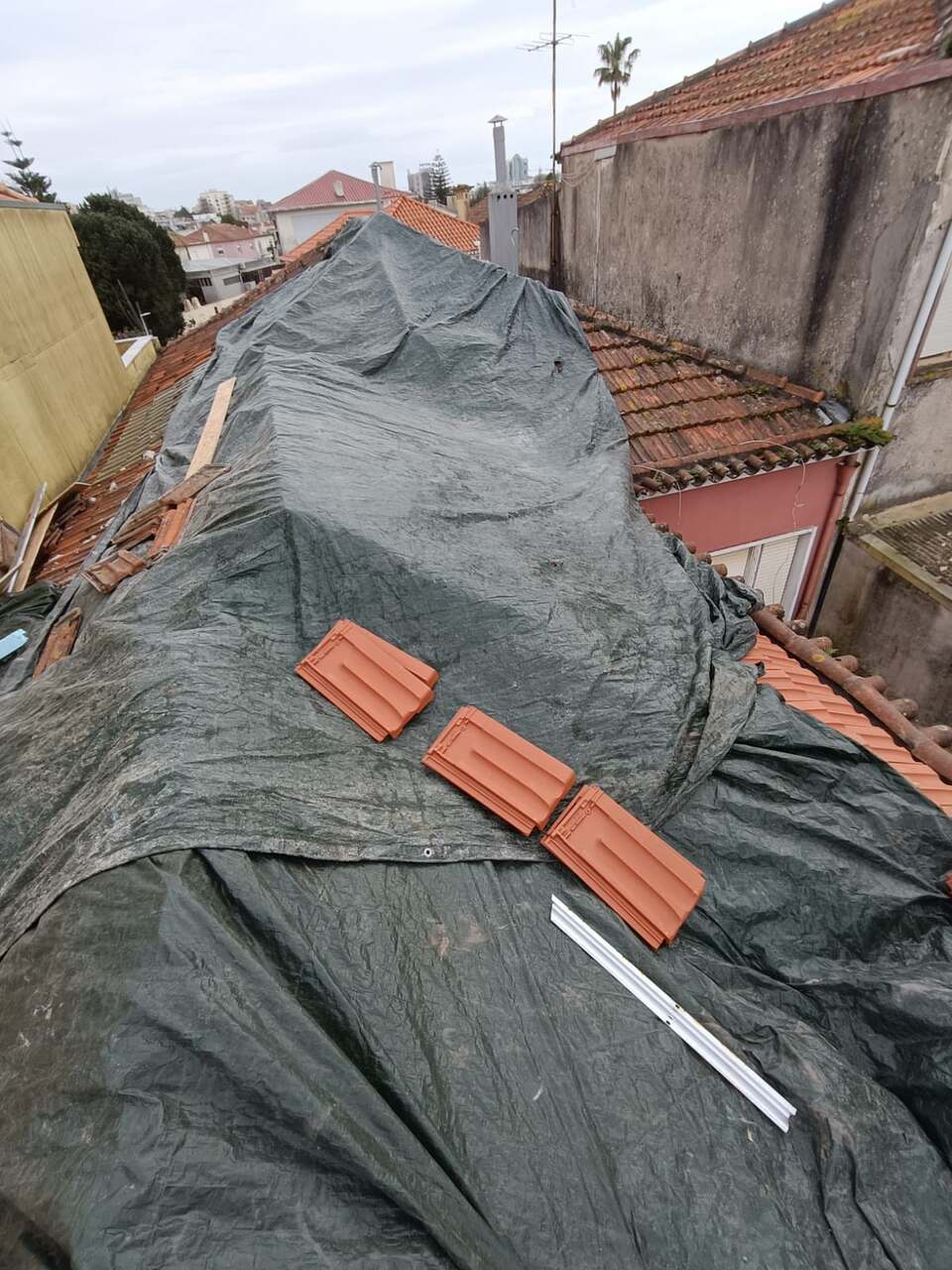 Telhado coberto com lona impermeável durante a obra, telhas novas ao lado
