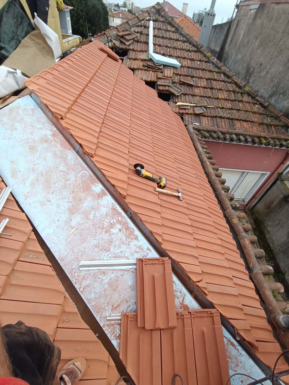 Telhado a meio da renovação — telha antiga com líquenes de um lado, telha nova do outro